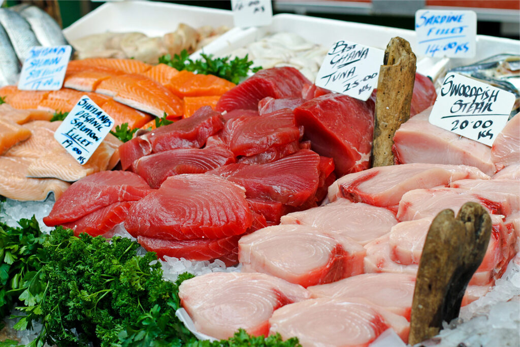 Un'esposizione di filetti di salmone fresco e tranci di tonno rosso brillante su ghiaccio con un cartello scritto a mano.